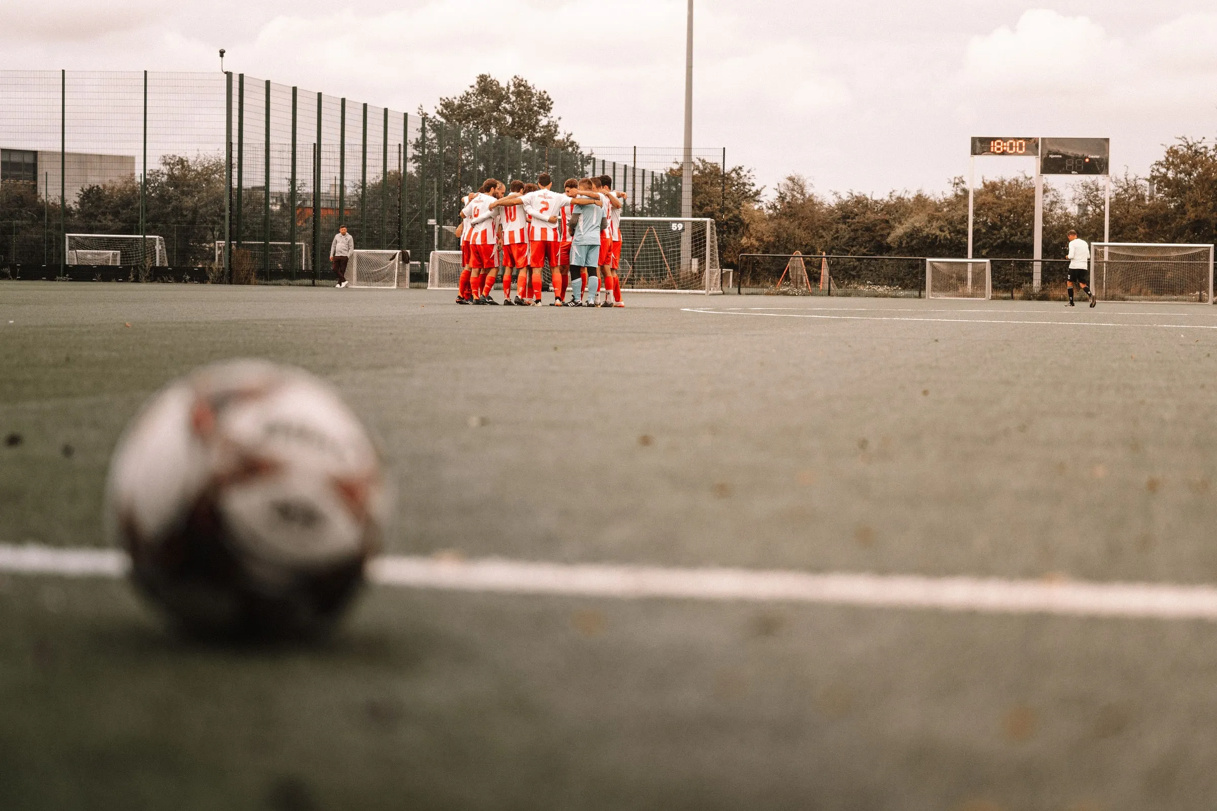A ball on the touchline with the team in a huddle on the pitch behind it